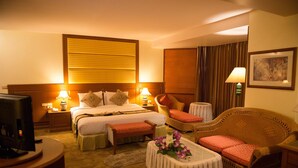 Una camera d'albergo con un letto, comodini, una televisione, un divano, un tavolino con fiori e un quadro appeso al muro.