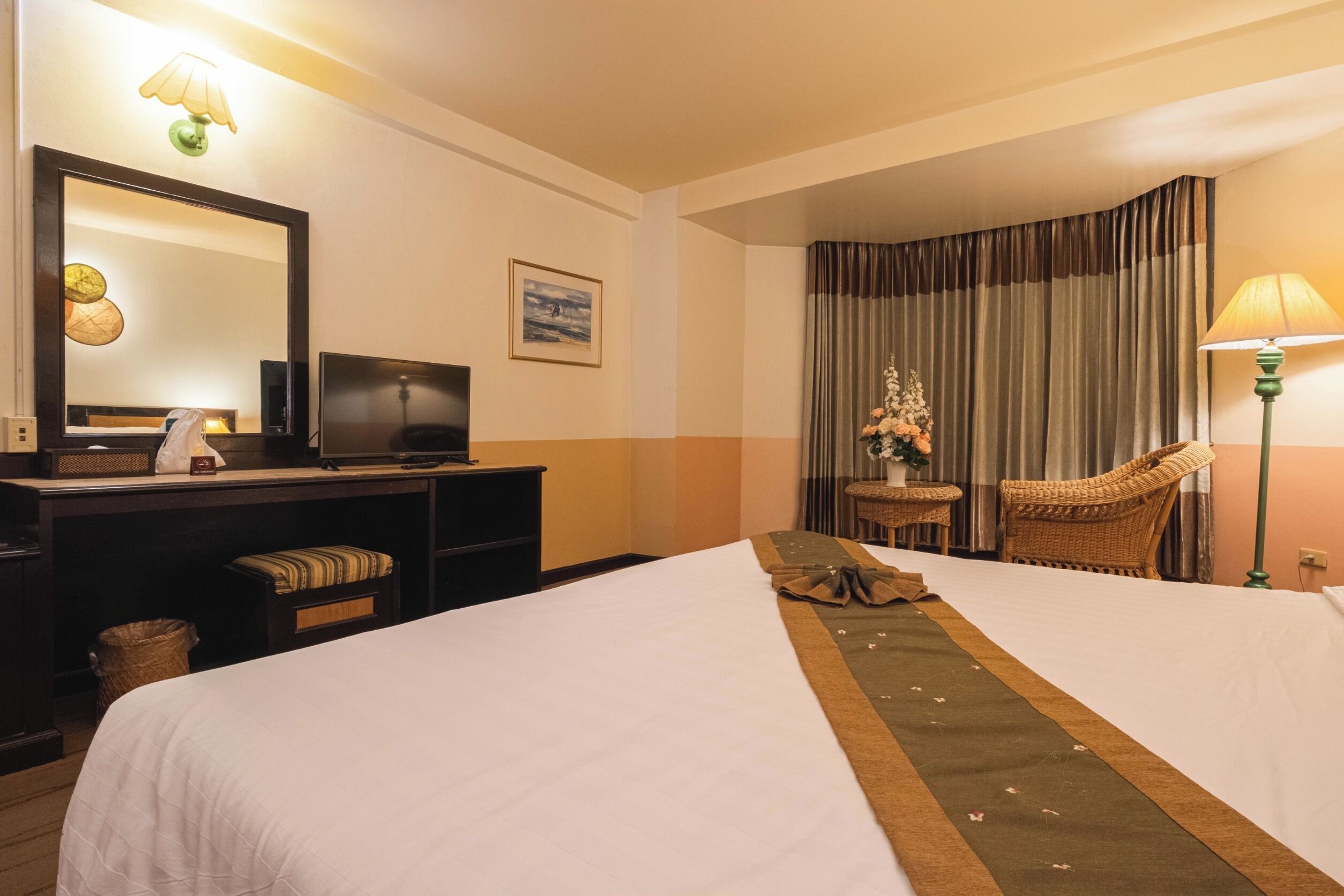 Habitación de hotel con dos camas, un escritorio con televisor, una silla, una lámpara y una ventana con cortinas.