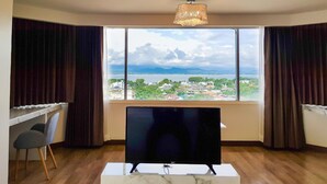 Una stanza con una grande finestra, una TV a schermo piatto, una scrivania e una sedia.