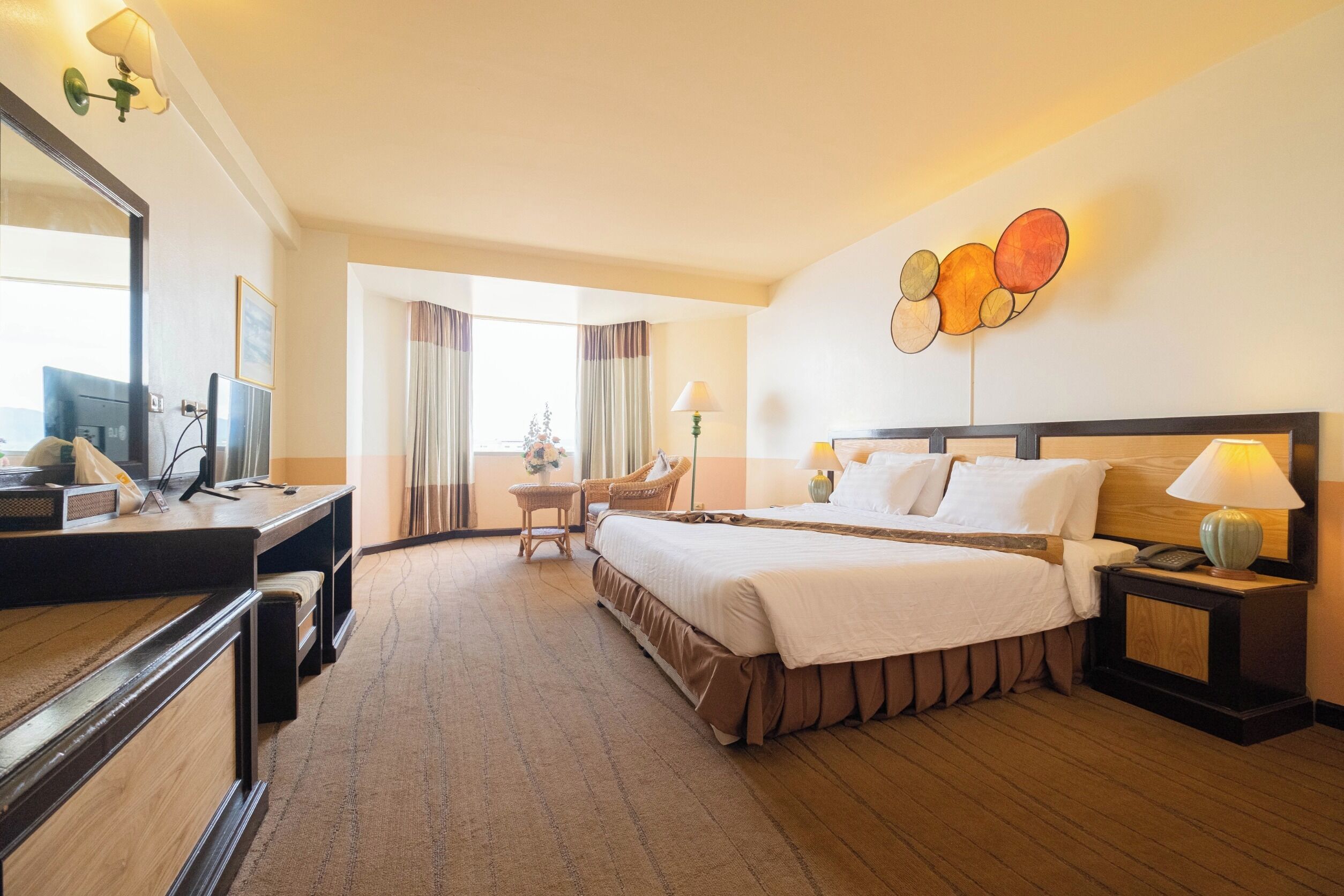 A hotel room with a bed, bedside table, lamp, and a desk with a computer.