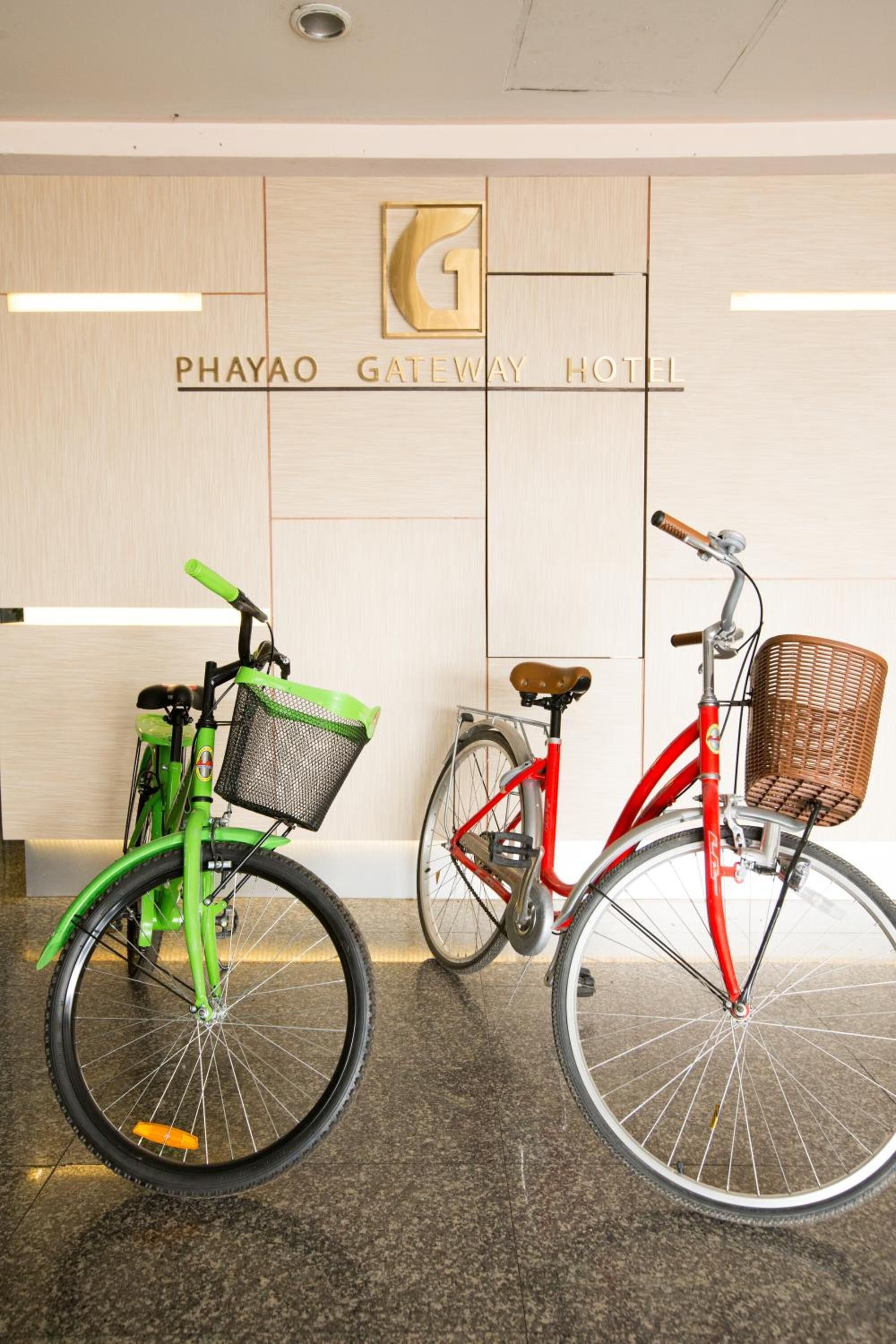 Two bicycles parked in front of a hotel entrance with a wooden facade and a sign that reads "PHAYAO GATEWAY HOTEL".