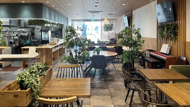 Un intérieur de restaurant moderne avec des tables et des chaises en bois, un espace cuisine et des plantes en pot.