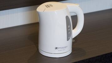 Chaleira elétrica branca sobre uma superfície de madeira, com etiqueta indicando que é da Green Rich Hotels e fabricada pela DRETEC.