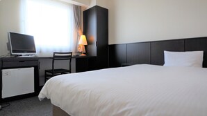 Une chambre d’hôtel équipée d’un lit, d’un bureau avec un ordinateur, d’une chaise, d’une lampe et d’un petit réfrigérateur.