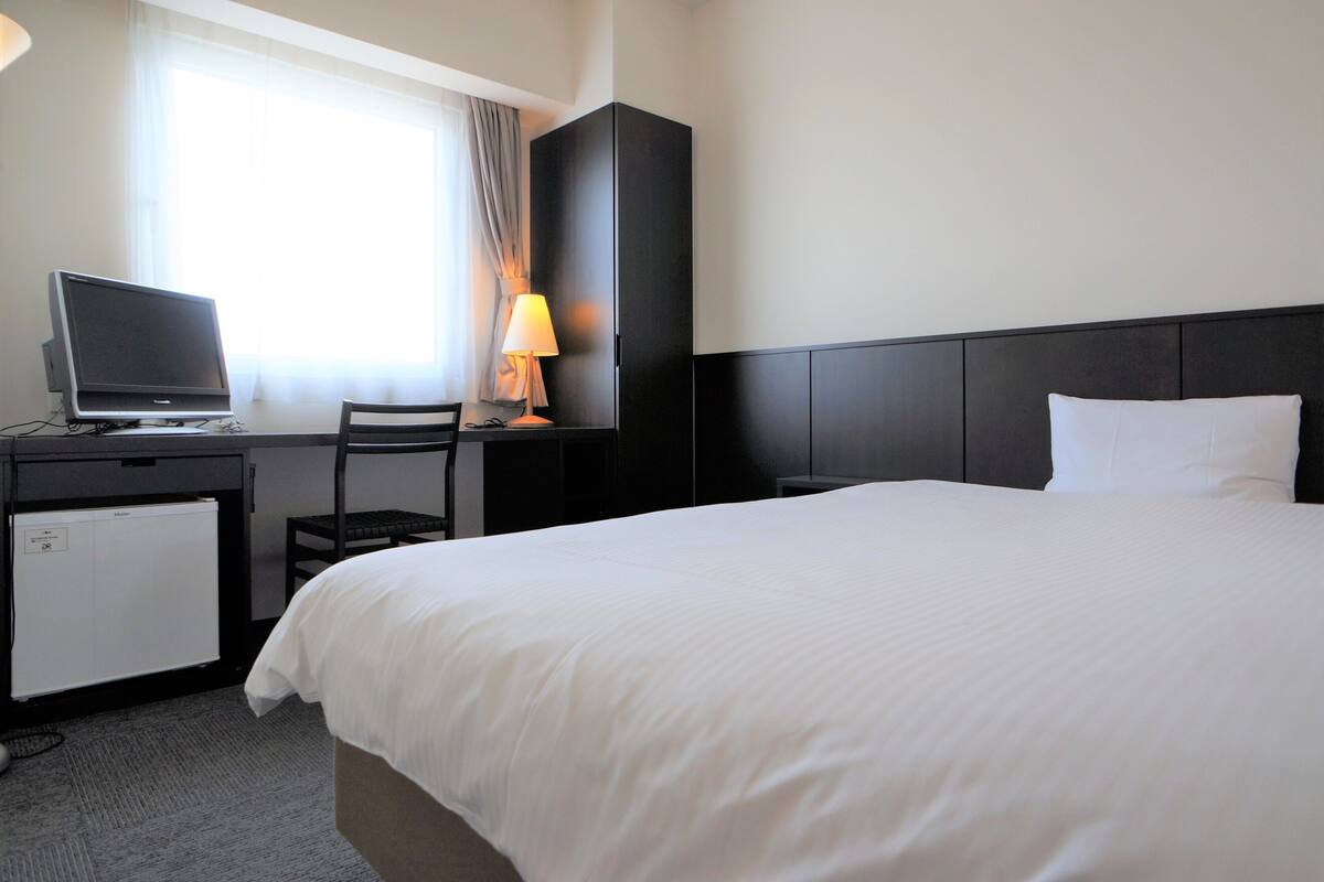 Une chambre d’hôtel équipée d’un lit, d’un bureau avec un ordinateur, d’une chaise, d’une lampe et d’un petit réfrigérateur.