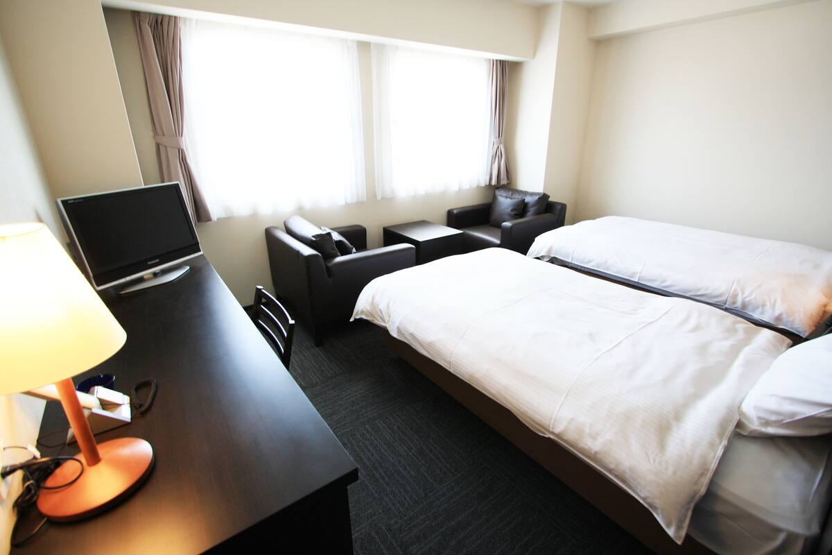 Une chambre d’hôtel avec un lit, un bureau avec un ordinateur portable, une chaise et une lampe.