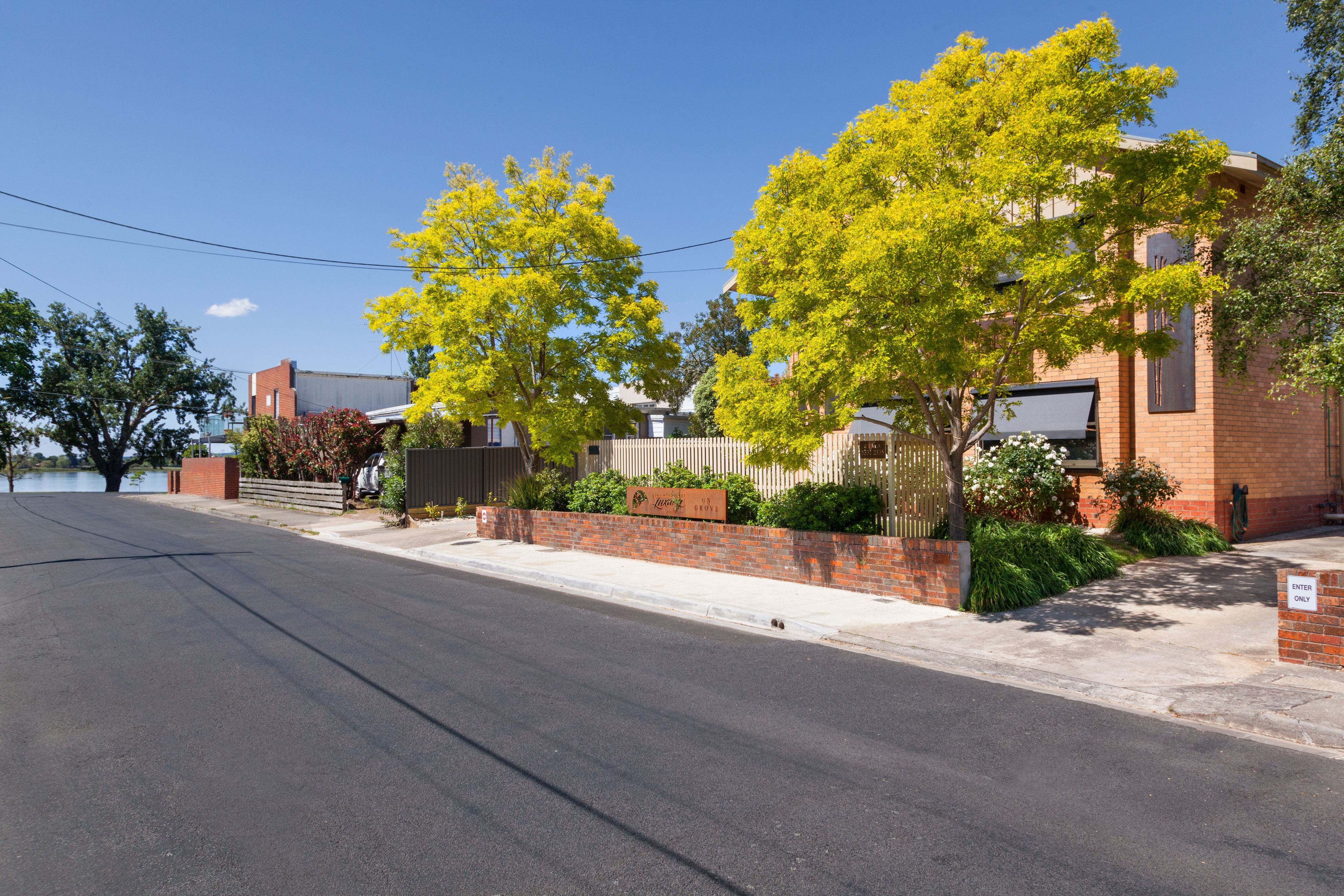 A residential street with a brick house, a fenced yard, and a clear sky.