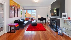 A modern living room with a black leather sofa, a red rug, and a flat-screen TV mounted on the wall.