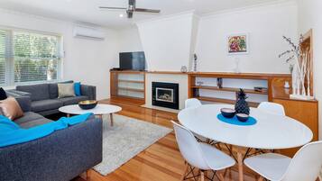 A modern living room with a grey sofa, white chairs, a round table, and a fireplace.