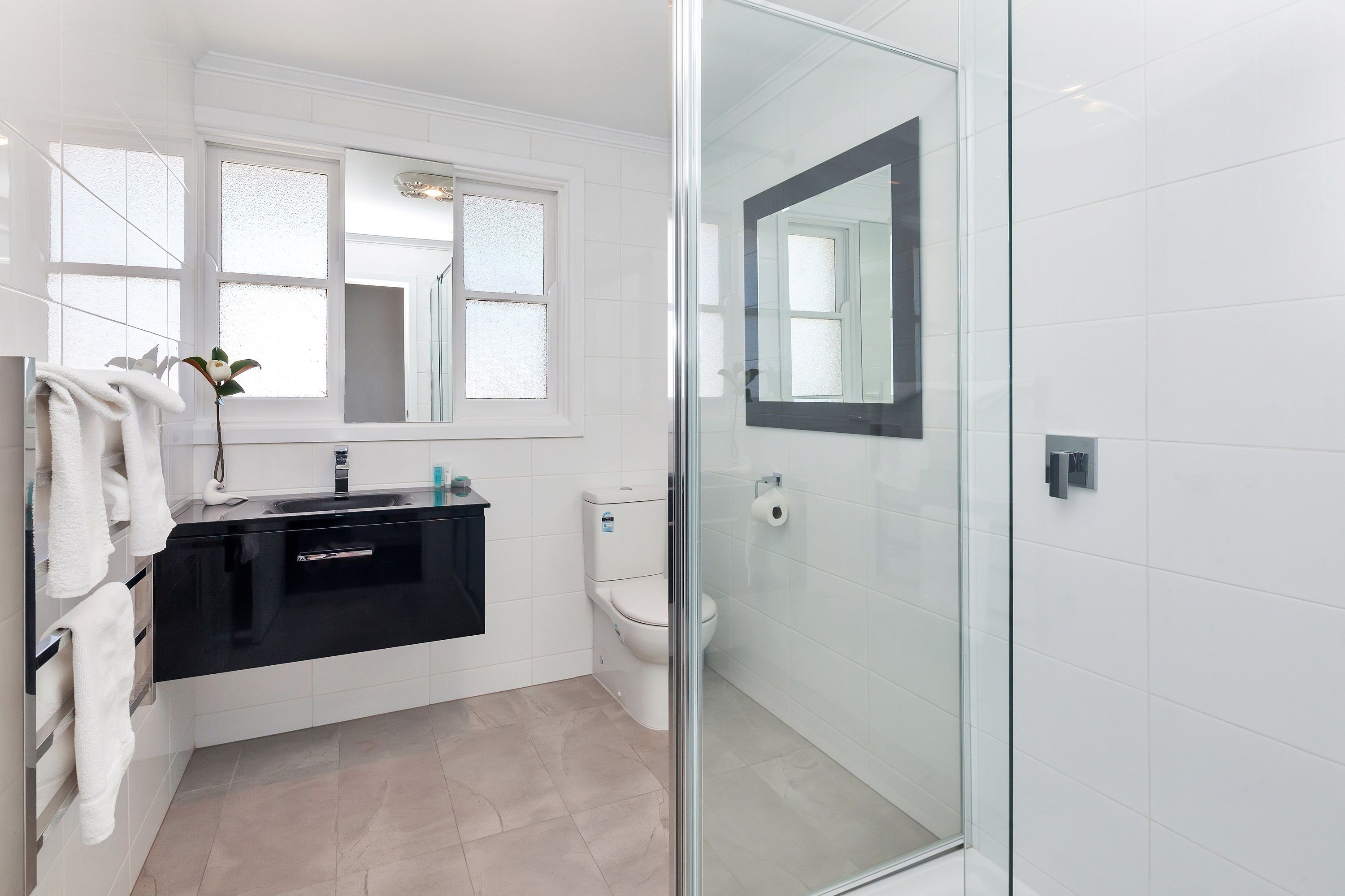 A modern bathroom with a glass shower enclosure, a white toilet, and a black vanity with a mirror.