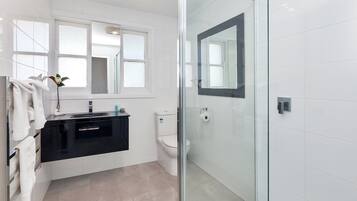 A modern bathroom with a glass shower enclosure, a white toilet, and a black vanity with a mirror.