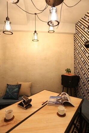 A cozy room with a wooden table, two chairs, a small black speaker, a magazine, a coffee cup, and a plant on a side table. - Just Hotel Jordan (Kowloon)