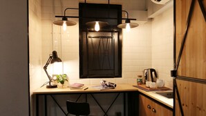 Et lille køkken med en træbordplade, en sort metalstol, en hængende lampe og et vægmonteret skab.