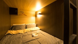 Et soveværelse med træloft, en seng med et tæppe, et væghængt knagerum og en lampe monteret på væggen.