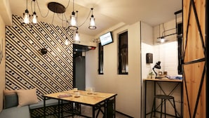 Et moderne hotelværelse med et mønstret væg, et træskrivebord, en barkrak og et siddeområde med puder.