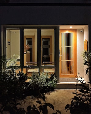 A modern building with a glass entrance, a wooden door with a metal gate, and potted plants in the foreground. - Benri sriracha residence (Si Racha)