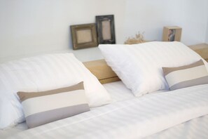 A neatly made bed with white bedding and two pillows, a wooden headboard, and a wall with two framed pictures. - Benri sriracha residence (Si Racha)