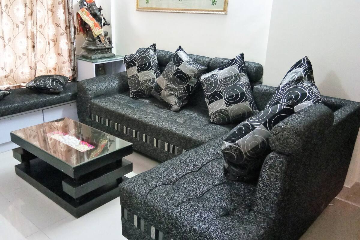 Ein modernes Wohnzimmer mit einem dunkelgrauen Sofa, gemusterten Kissen und einem Glastisch.