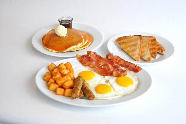 Un plato de desayuno con tortitas, tocino, huevos, patatas ralladas y tostadas.