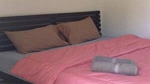 A bed with a pink blanket and two brown pillows.