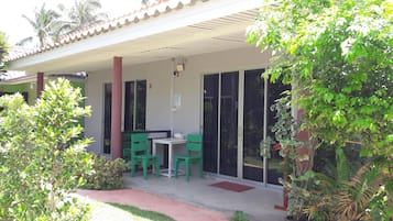 A covered outdoor seating area with a table and chairs, a door, and a small garden with plants.