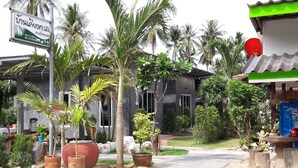 A building with a signboard, surrounded by various potted plants and palm trees.