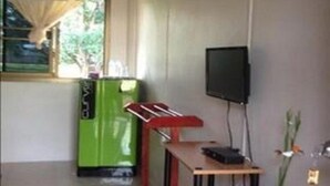 A room with a green refrigerator, a wooden table, a flat-screen TV mounted on the wall, and a window with curtains.