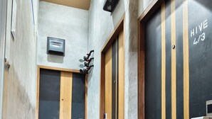 A narrow hallway with tiled flooring, wooden and black doors, and a ceiling-mounted air conditioning unit. - Hive28 (Bangkok)