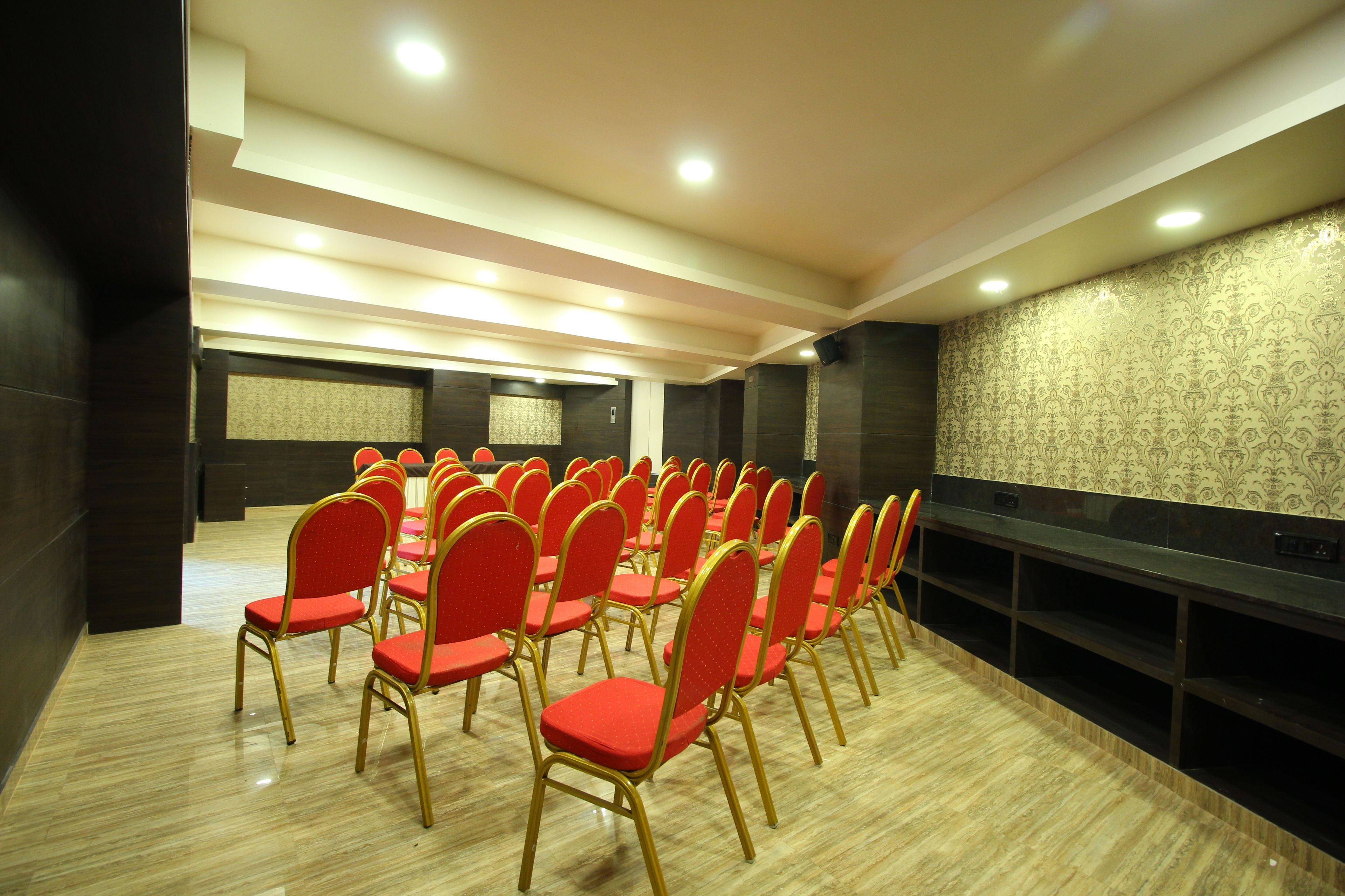 A conference room with rows of red chairs, a large screen, and a patterned wall.