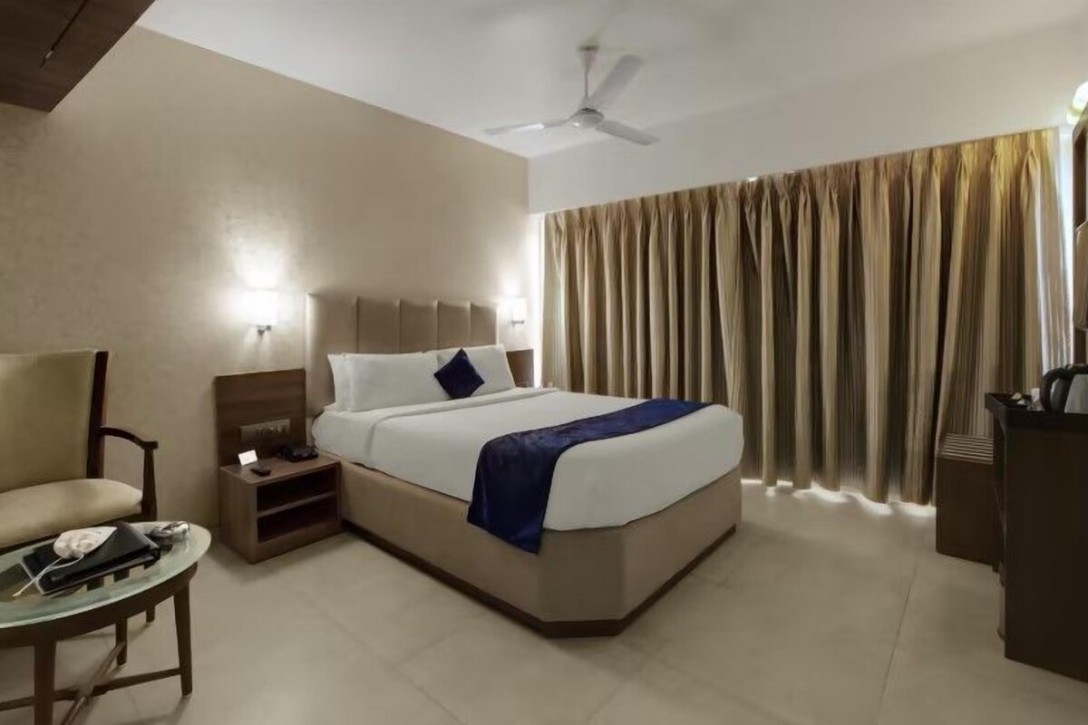 Una habitación de hotel con una cama, una silla, un escritorio, un televisor y un ventilador de techo.
