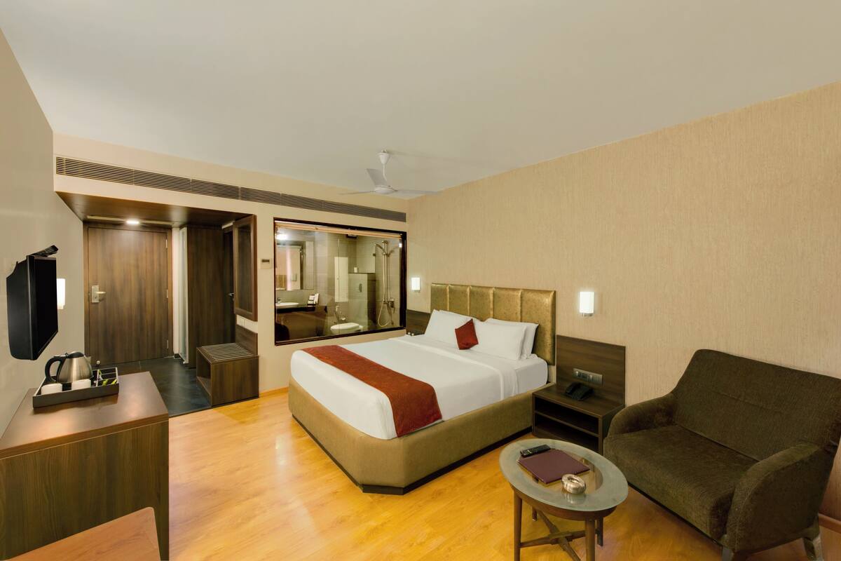 A hotel room with a large bed, a sitting area with a sofa and a small table, a TV, and a mirror.