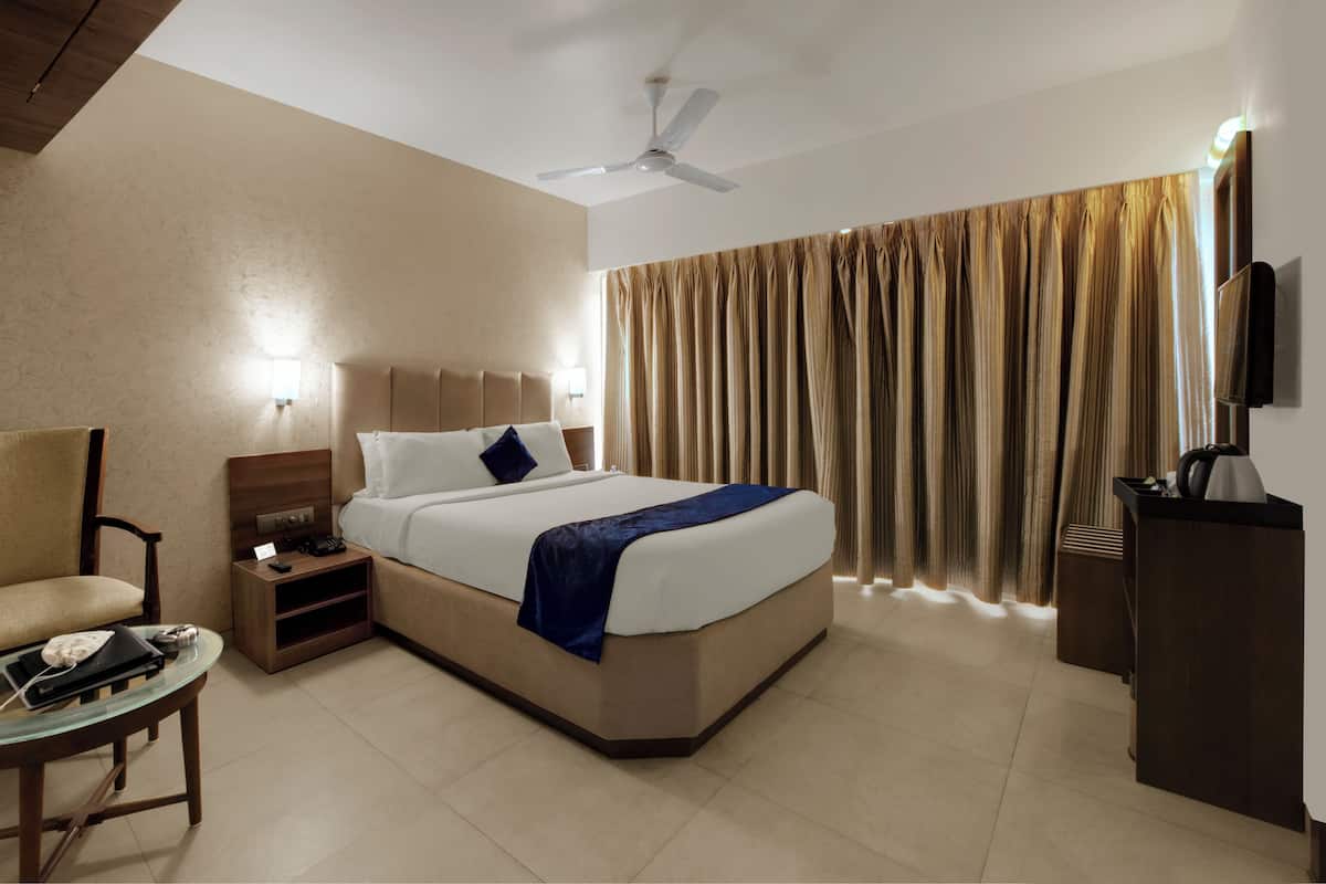 A hotel room with a bed, a chair, a bedside table, a TV, and a ceiling fan.