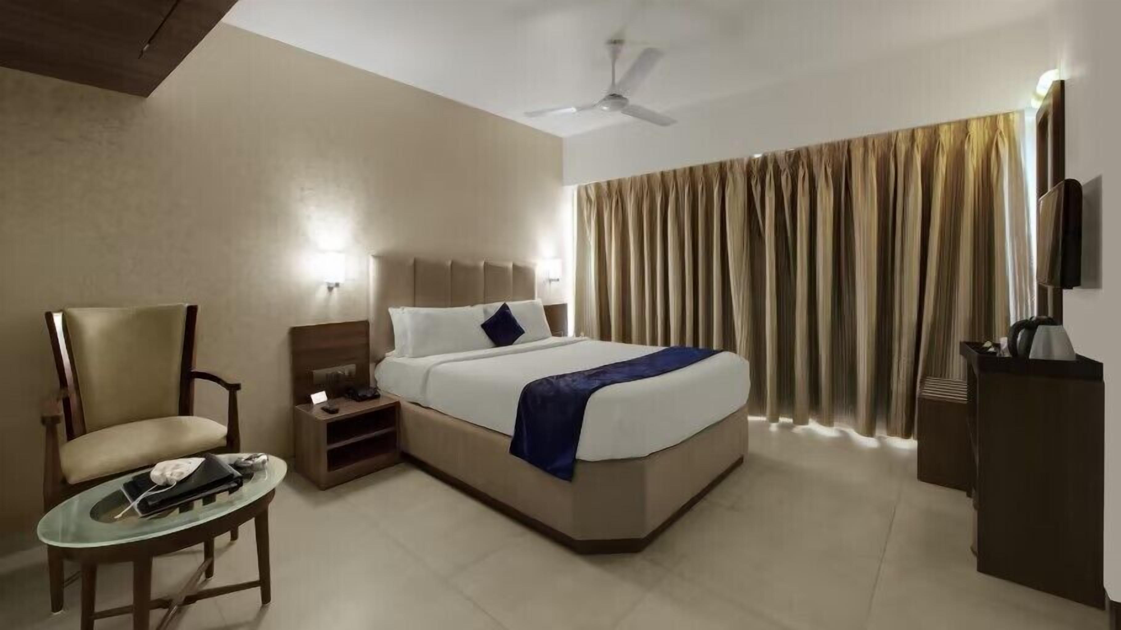 A hotel room with a bed, a chair, a desk, a television, and a ceiling fan.
