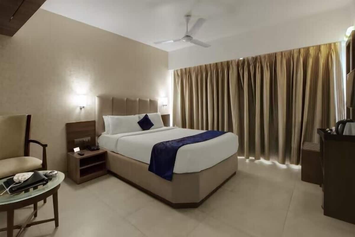 A hotel room with a bed, a chair, a desk, a television, and a ceiling fan.