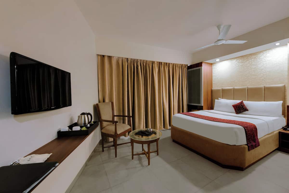 A hotel room with a bed, a television, a chair, a small table, and curtains.