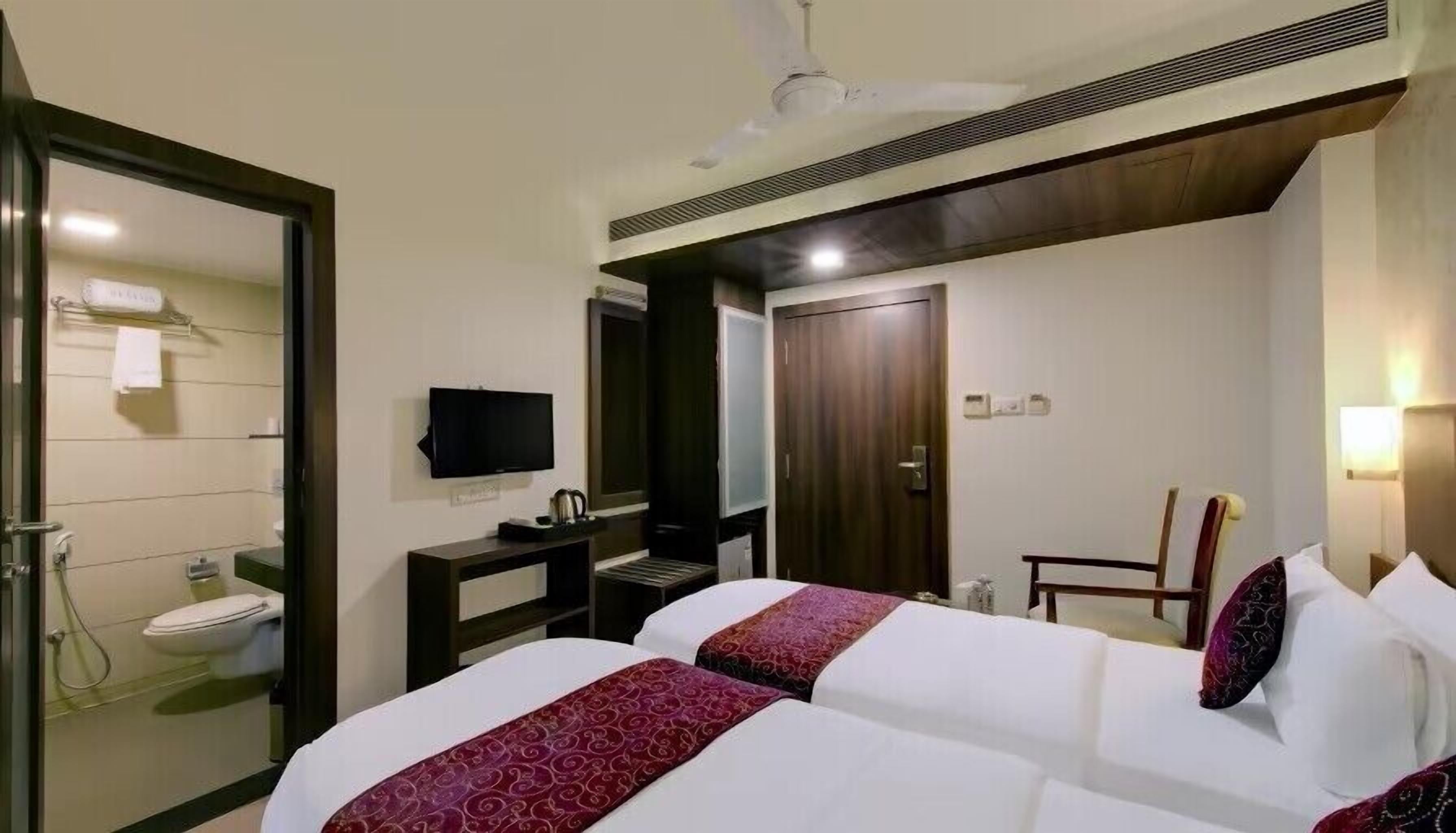 A hotel room with two beds, a TV, a desk, a chair, a wardrobe, and a bathroom.