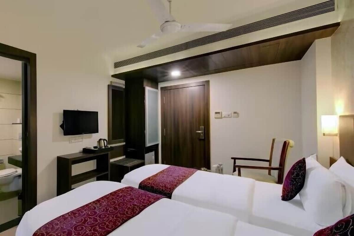 A hotel room with two beds, a TV, a desk, a chair, a wardrobe, and a bathroom.