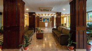 Um hall com pilares de madeira, sofás e plantas em vasos.