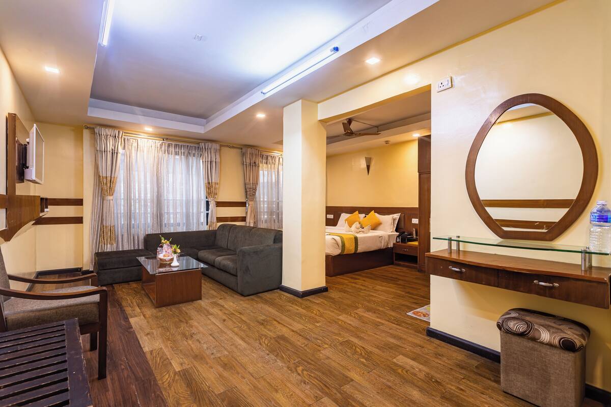 Habitación de hotel con sofá, cama, mesa de centro de vidrio, suelo de madera y un espejo grande.