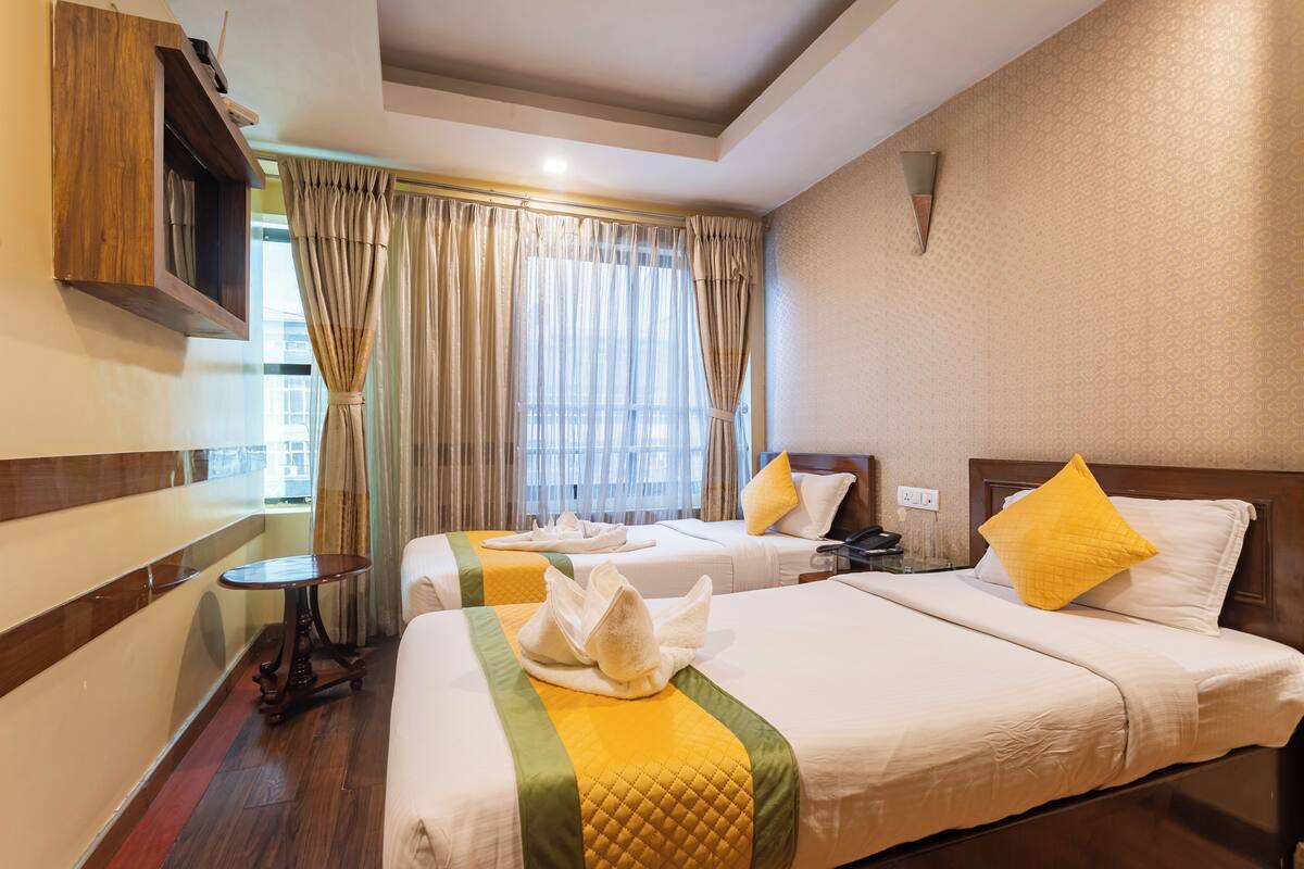 Habitación de hotel con dos camas, cabecero de madera, una mesita y una ventana con cortinas.