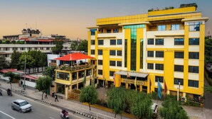 Um edifício amarelo com vários andares, um restaurante no andar térreo e uma bandeira visível.