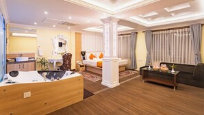 Quarto de hotel moderno com piso de madeira, área de estar com sofá e mesa de centro, espelho grande e mesa de jantar com cadeiras.