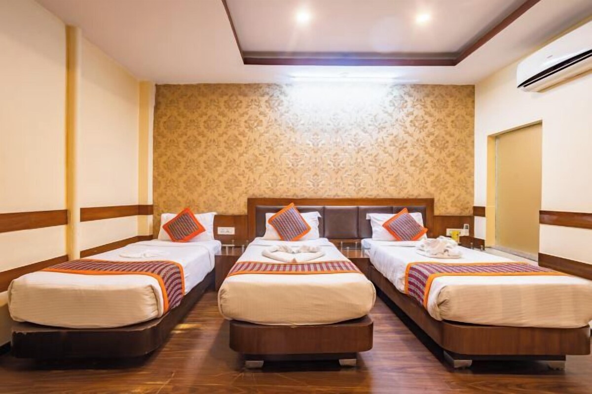A hotel room with three beds, each with a wooden headboard, white bedding, and orange accents.