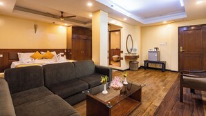 Quarto de hotel com cama, sofá, mesa de centro e uma pequena cozinha equipada.