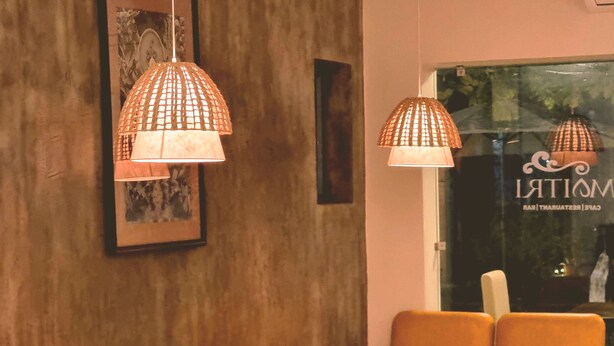 A seating area with orange chairs and white tables, a framed picture on the wall, and hanging lamps. - Hotel Ananda Inn (Lumbini)