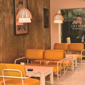A seating area with orange chairs and white tables, a framed picture on the wall, and hanging lamps. - Hotel Ananda Inn (Lumbini)