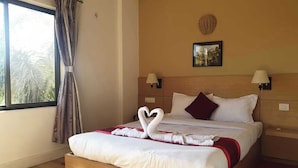 A hotel room with a bed, two bedside lamps, a wall-mounted picture, and a window with curtains. - Hotel Ananda Inn (Lumbini)