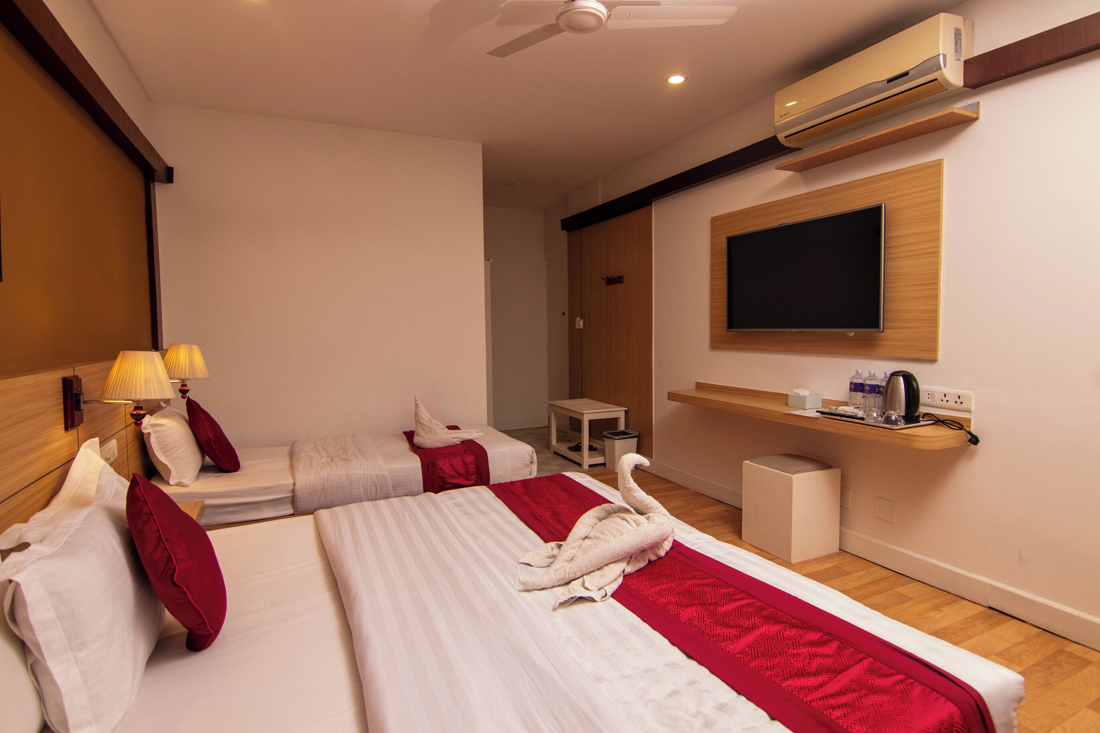 A hotel room with two beds, a TV, an air conditioner, and a small table with a kettle.