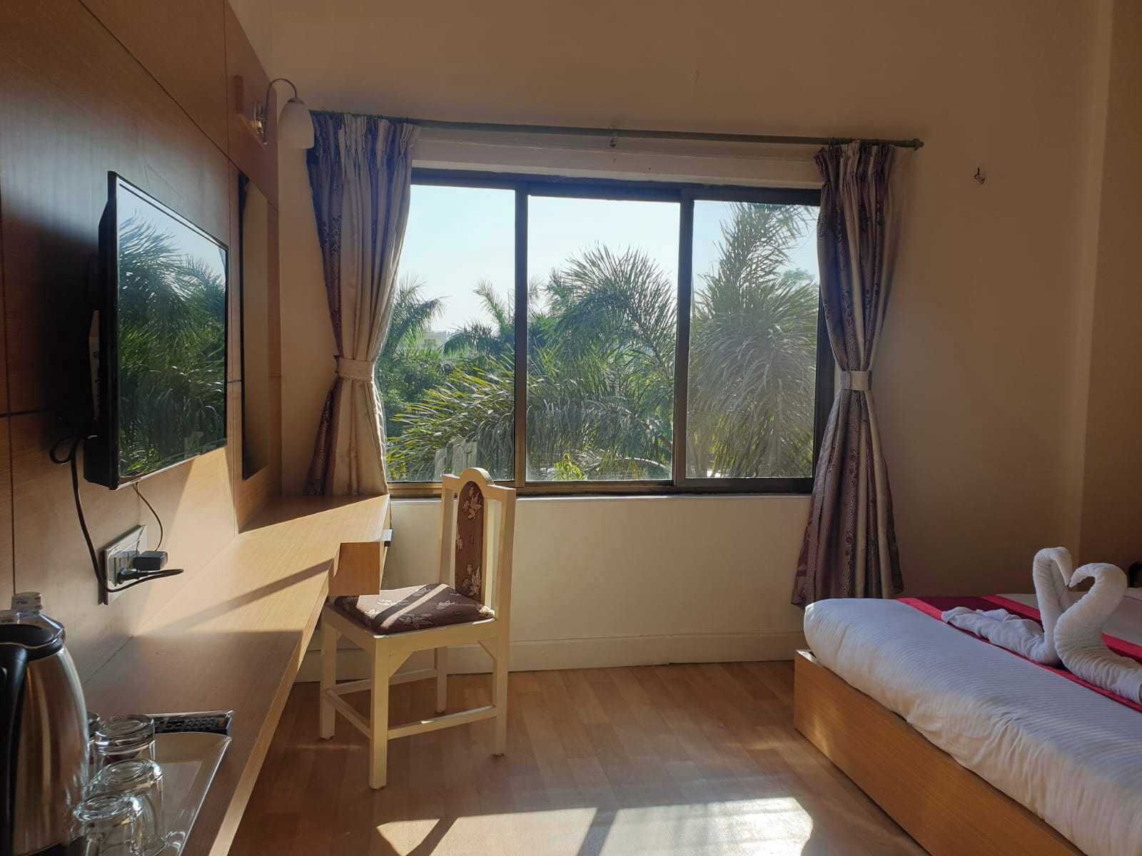 Una stanza con un letto, una televisione a parete, una sedia e una finestra con tende.