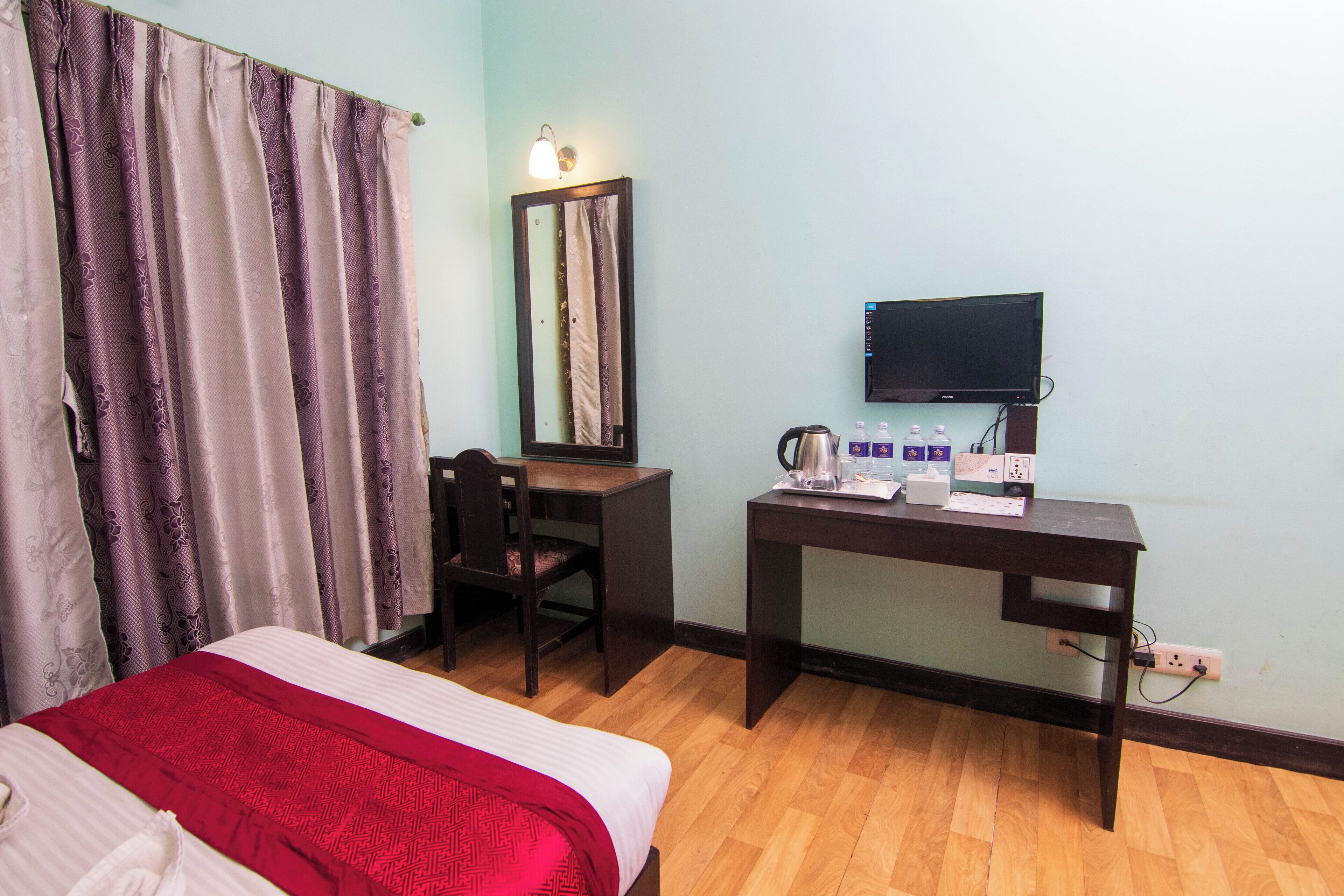 A hotel room with a bed, a desk with a chair, a television, and a mirror.